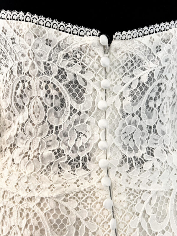 Robe de mariée en dentelle à manches trois-quarts avec détails floraux, avec une mariée élégante en pleine conversation avec un homme en costume beige