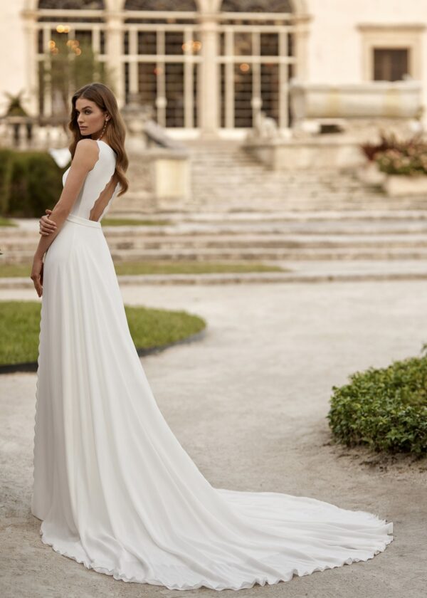 Mariée de dos portant une robe de mariée avec dos ouvert en forme de vague et longue traîne, posant devant un bâtiment historique
