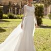 Mariée souriante portant une robe élégante avec un haut en dentelle à manches longues et une jupe fluide, se tenant dans un jardin ensoleillé