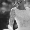 Portrait en noir et blanc d'une mariée rayonnante portant une robe en dentelle à manches longues, capturée en plein sourire