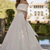 Mariée élégante portant une robe avec un corsage en dentelle et un drapé asymétrique aux épaules, dans un cadre extérieur luxueux