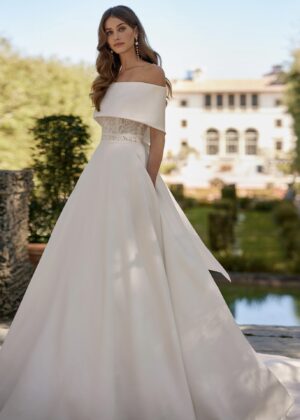 Mariée élégante portant une robe avec un corsage en dentelle et un drapé asymétrique aux épaules, dans un cadre extérieur luxueux