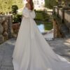 Vue de dos d'une mariée portant une robe volumineuse avec manches bouffantes et un nœud élégant, dans un jardin majestueux