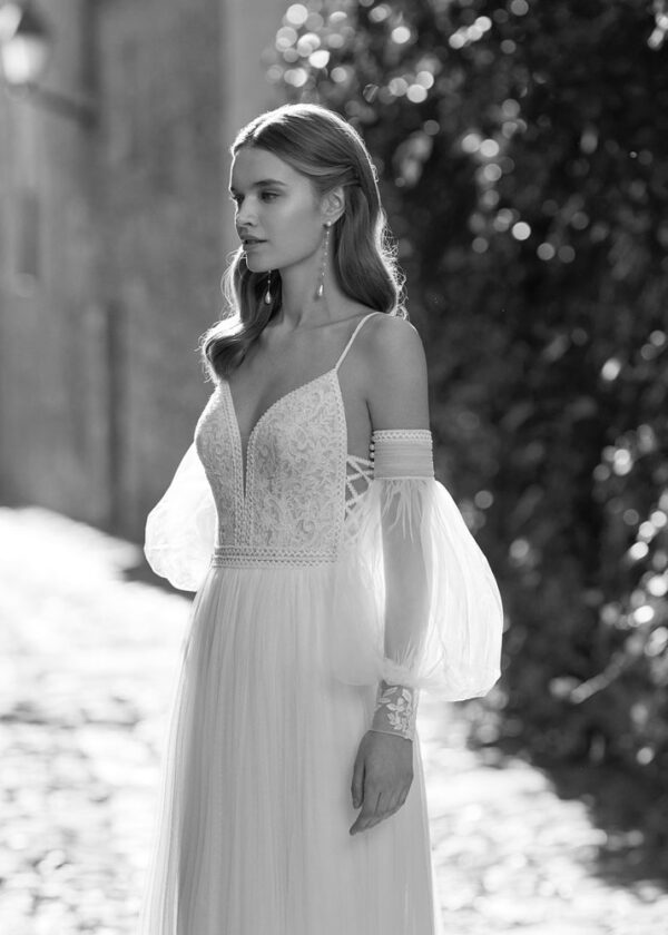 Portrait en noir et blanc d'une mariée portant une robe de mariée fluide avec un décolleté en V, des manches bouffantes et des détails en dentelle