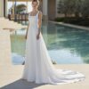 Une mariée portant une robe de mariée blanche avec une coupe droite et un col carré, posant élégamment devant une piscine à l'architecture classique.