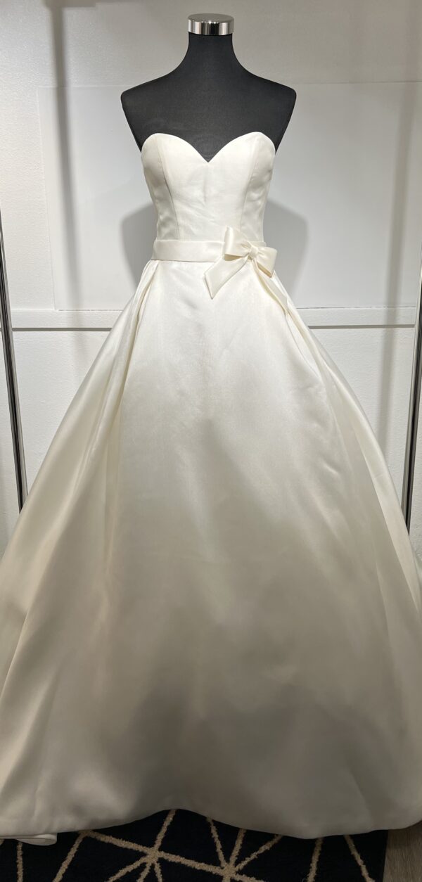 Robe de mariée Divina Sposa coupe princesse en satin blanc, bustier cœur sans bretelles, ceinture à nœud et jupe fluide jusqu’au sol.