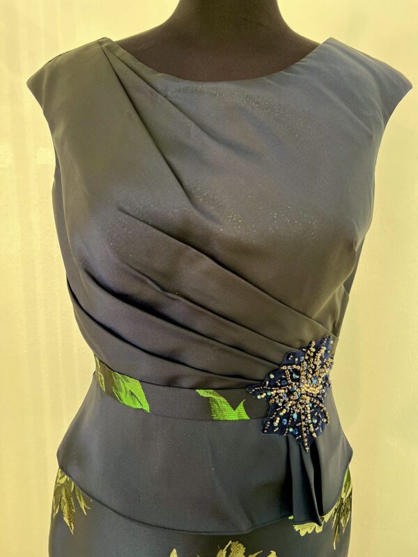 Robe longue bleu marine avec motif floral doré et vert, encolure bateau et jupe sirène évasée, ceinture ornée de sequins.