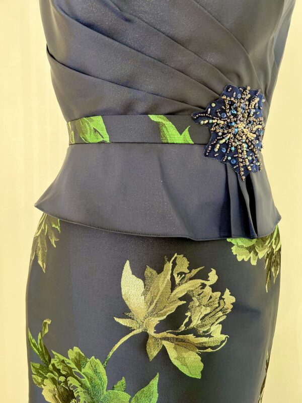 Robe longue bleu marine avec motif floral doré et vert, encolure bateau et jupe sirène évasée, ceinture ornée de sequins.