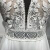 Robe de mariée avec bustier en tulle illusion, broderies florales blanches, décolleté en dentelle et manches cap.