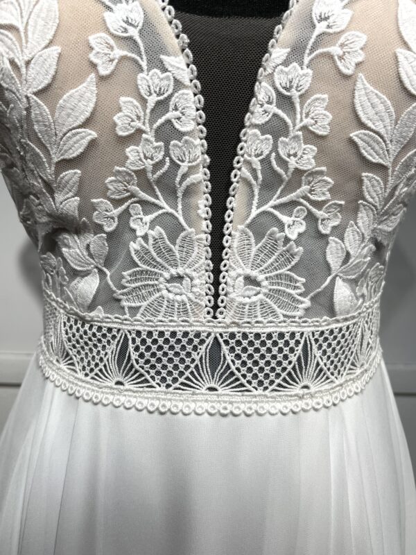 Robe de mariée avec bustier en tulle illusion, broderies florales blanches, décolleté en dentelle et manches cap.