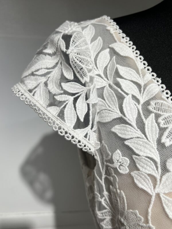 Robe de mariée avec bustier en tulle illusion, broderies florales blanches, décolleté en dentelle et manches cap.