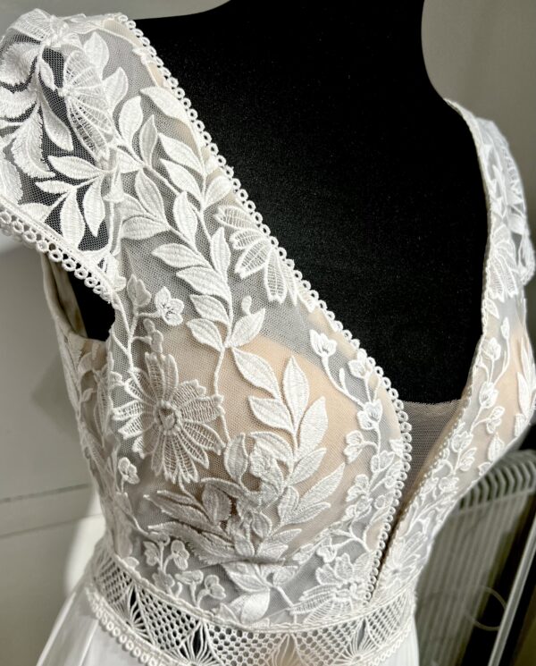 Robe de mariée avec bustier en tulle illusion, broderies florales blanches, décolleté en dentelle et manches cap.