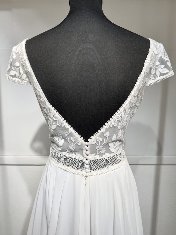 Robe de mariée avec bustier en tulle illusion, broderies florales blanches, décolleté en dentelle et manches cap.