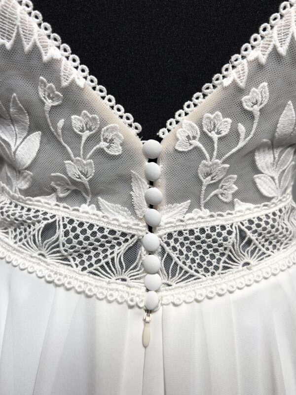 Robe de mariée avec bustier en tulle illusion, broderies florales blanches, décolleté en dentelle et manches cap.