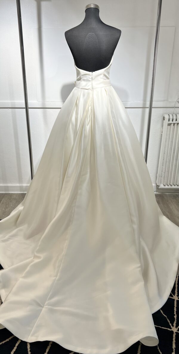 Robe de mariée Divina Sposa coupe princesse en satin blanc, bustier cœur sans bretelles, ceinture à nœud et jupe fluide jusqu’au sol.