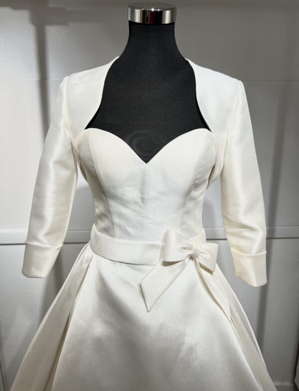 Robe de mariée Divina Sposa coupe princesse en satin blanc, bustier cœur sans bretelles, ceinture à nœud et jupe fluide jusqu’au sol.