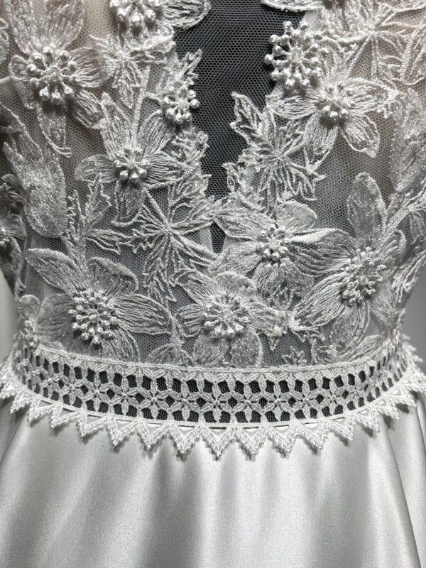 La robe de mariée Tiara avec décolleté en V, bustier en dentelle, ceinture perlée et jupe fluide en satin