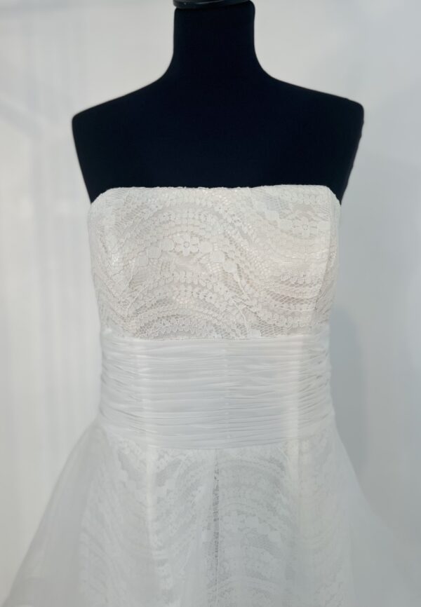 Robe de mariée bustier en tulle blanc, corsage texturé, volants superposés et base légèrement transparente, pour une silhouette aérienne et romantique.