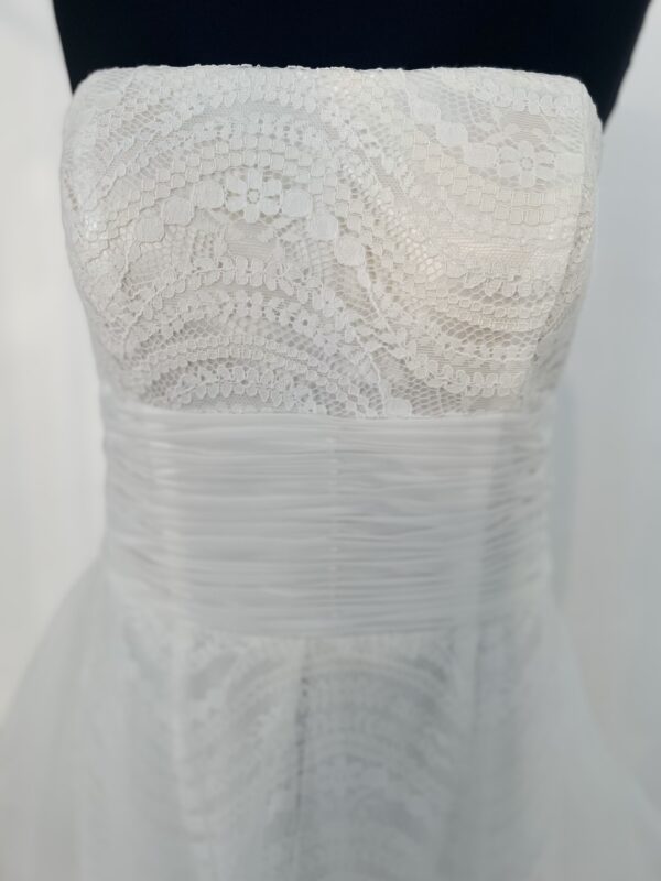 Robe de mariée bustier en tulle blanc, corsage texturé, volants superposés et base légèrement transparente, pour une silhouette aérienne et romantique.