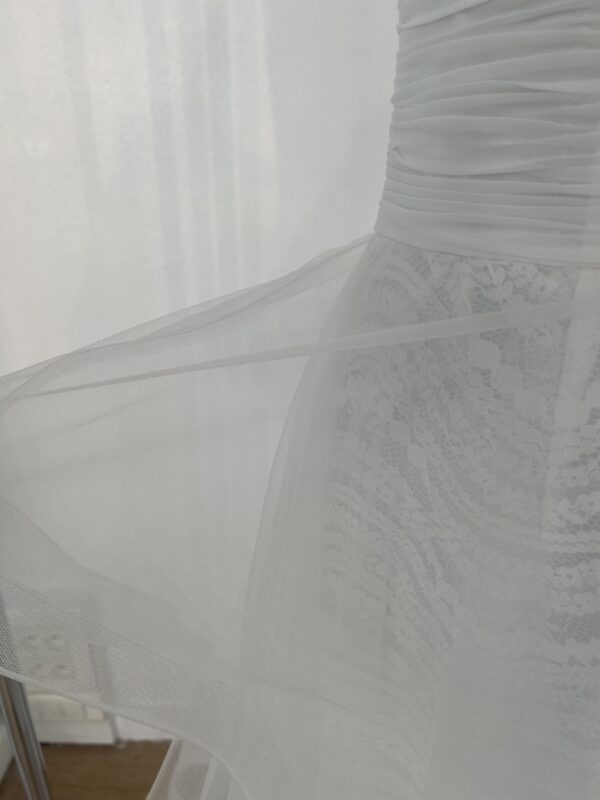 Robe de mariée bustier en tulle blanc, corsage texturé, volants superposés et base légèrement transparente, pour une silhouette aérienne et romantique.