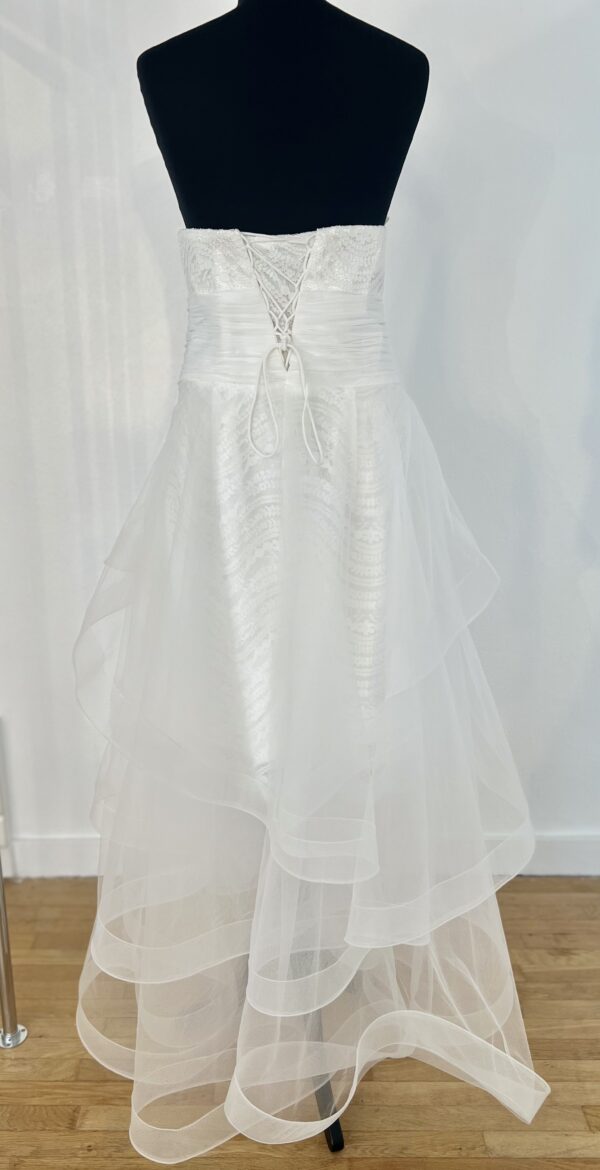 Robe de mariée bustier en tulle blanc, corsage texturé, volants superposés et base légèrement transparente, pour une silhouette aérienne et romantique.