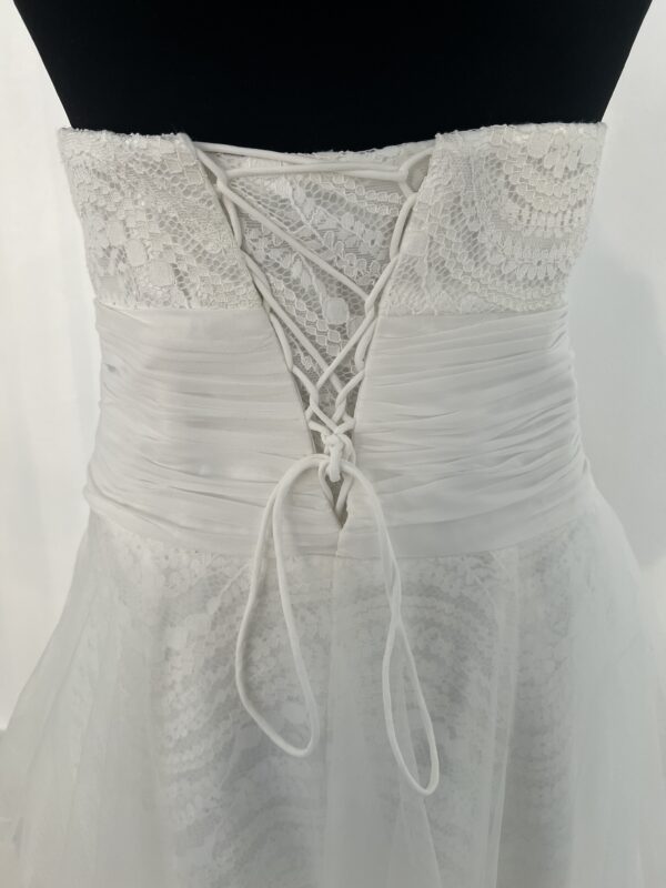Robe de mariée bustier en tulle blanc, corsage texturé, volants superposés et base légèrement transparente, pour une silhouette aérienne et romantique.