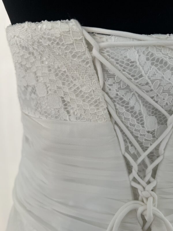 Robe de mariée bustier en tulle blanc, corsage texturé, volants superposés et base légèrement transparente, pour une silhouette aérienne et romantique.
