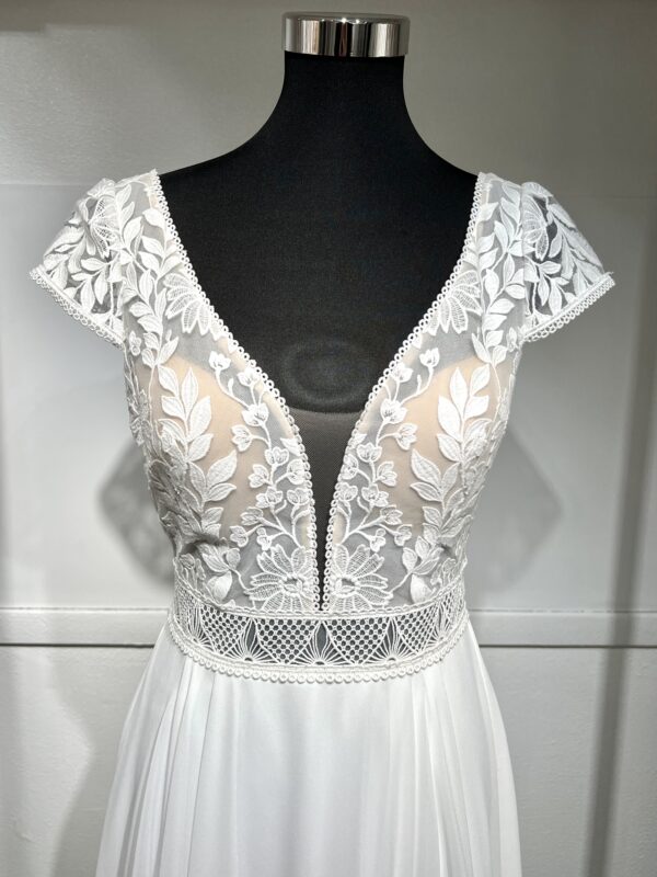 Robe de mariée avec bustier en tulle illusion, broderies florales blanches, décolleté en dentelle et manches cap.