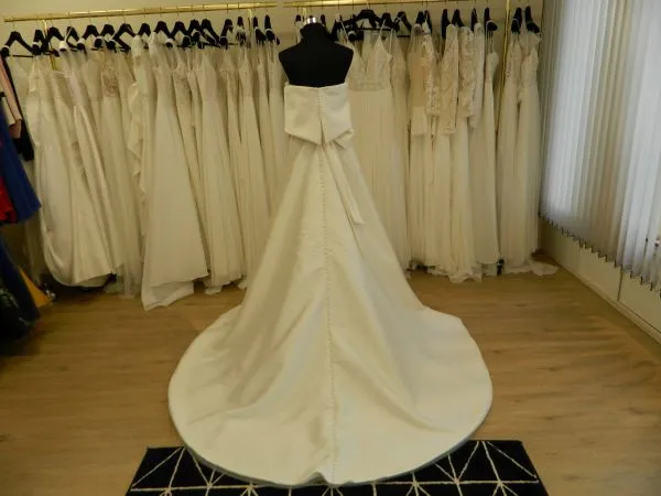 Robe de mariée princesse en mikado Syma par Aire Barcelona vue de dos avec traîne circulaire et grand nœud détachable.