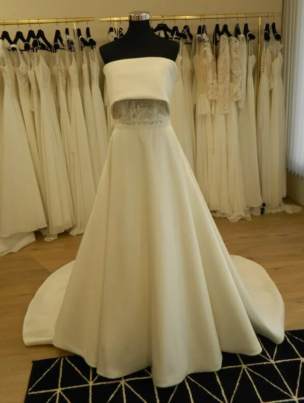 Robe de mariée princesse en mikado Syma par Aire Barcelona présentée de face sur portant en boutique.