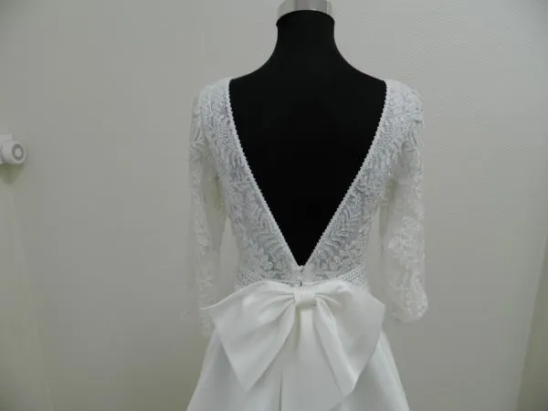 Gros plan sur le décolleté en V plongeant en dentelle brodée et le nœud en mikado du dos de la robe de mariée Suna d'Aire Barcelona.