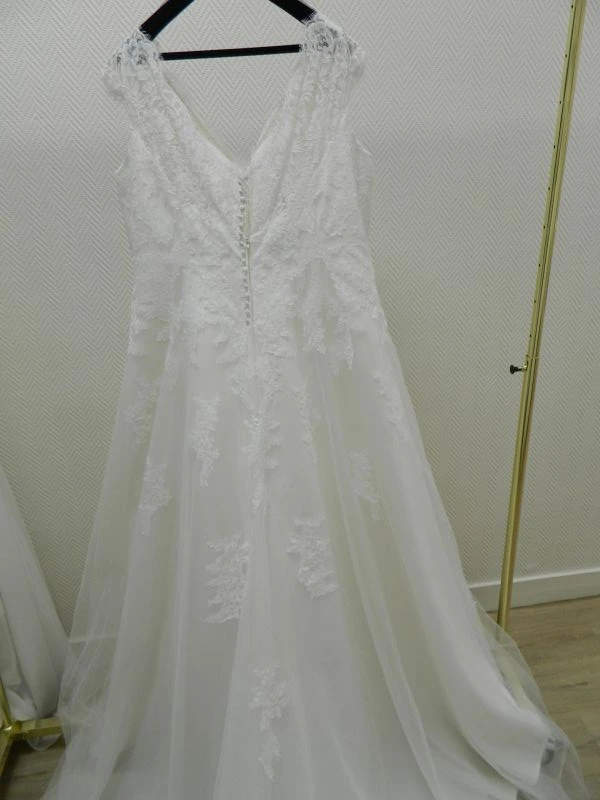 Robe de mariée princesse grande taille modèle 23805 par Curvy, vue de dos sur cintre avec grand décolleté en V, fine boutonnière et applications de dentelle florale descendant sur la jupe en tulle.