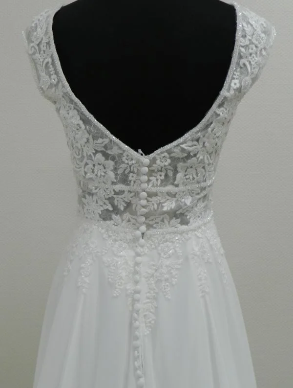 Gros plan technique de dos sur le décolleté en V plongeant, la longue rangée de boutons recouverts et le bustier en dentelle pailletée de la robe de mariée 44275 Justin Alexander.