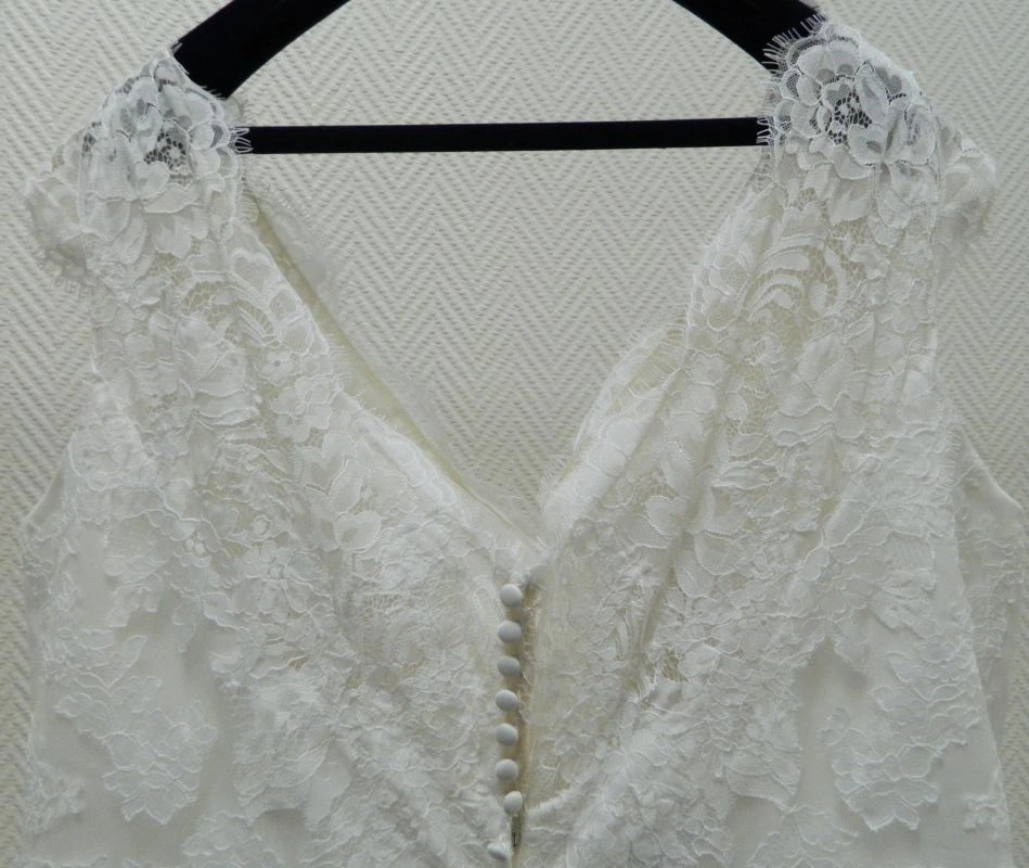 Gros plan macro sur la boutonnière blanche et le décolleté en V en dentelle de cils du dos de la robe de mariée grande taille 23805 de Curvy.