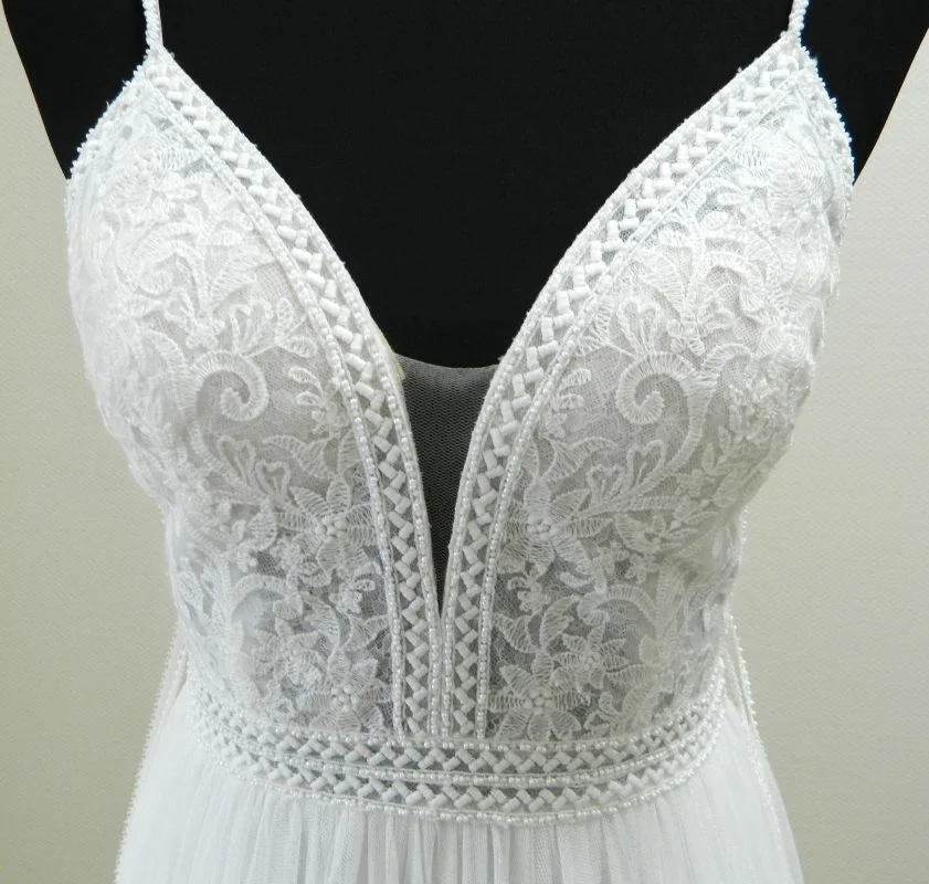 Gros plan technique sur le bustier en dentelle florale et le décolleté en V plongeant de la robe de mariée princesse Ululan de Rosa Clará.