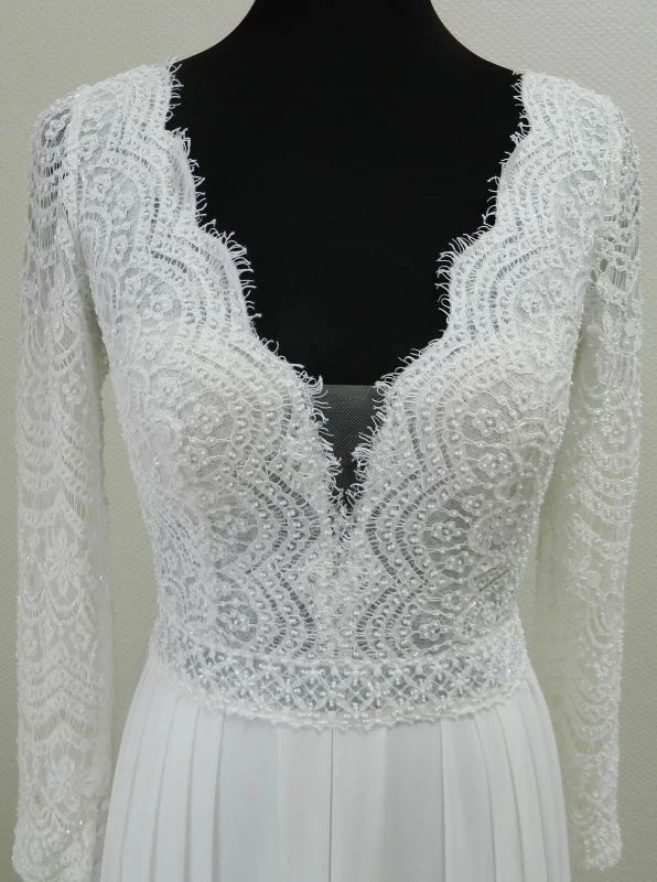Gros plan technique de face sur le bustier en dentelle géométrique et florale, le décolleté plongeant en V et les manches longues perlées de la robe de mariée Darcy de Rosa Clará.