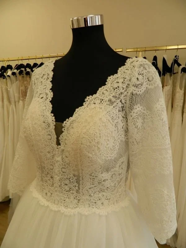 Gros plan technique de face sur le bustier en dentelle florale, l'encolure en V festonnée et les manches trois-quarts de la robe de mariée princesse 23711 de One and Only.