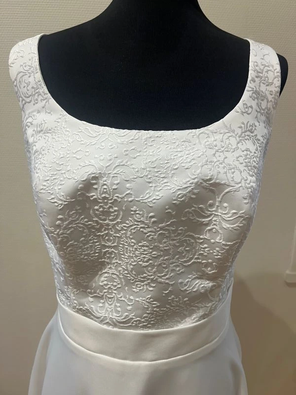 Gros plan sur le bustier en guipure baroque blanche et la ceinture de la robe de mariée courte Alessia par Allen Rich, présentée sur un mannequin.