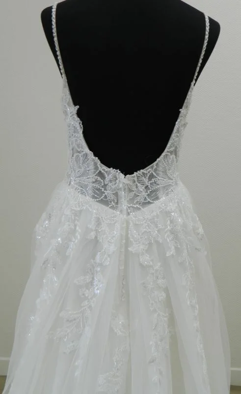Gros plan technique de dos sur le décolleté arrondi style dos nu, les fines bretelles perlées et la dentelle fleurie scintillante de la robe de mariée princesse 23236 Très Chic.