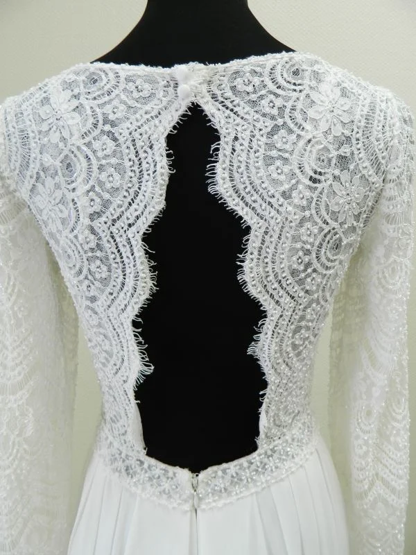 Gros plan technique de dos sur l'ouverture graphique en trou de serrure, les bordures de dentelle festonnée à franges cils et la taille perlée de la robe de mariée Darcy de Rosa Clará.