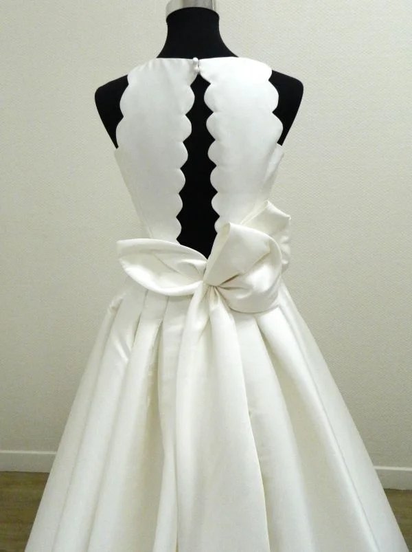 Gros plan sur le dos de la robe de mariée Evana de Rosa Clará, montrant le décolleté dos nu vertical bordé de grands festons arrondis et un gros nœud asymétrique en mikado à la taille.