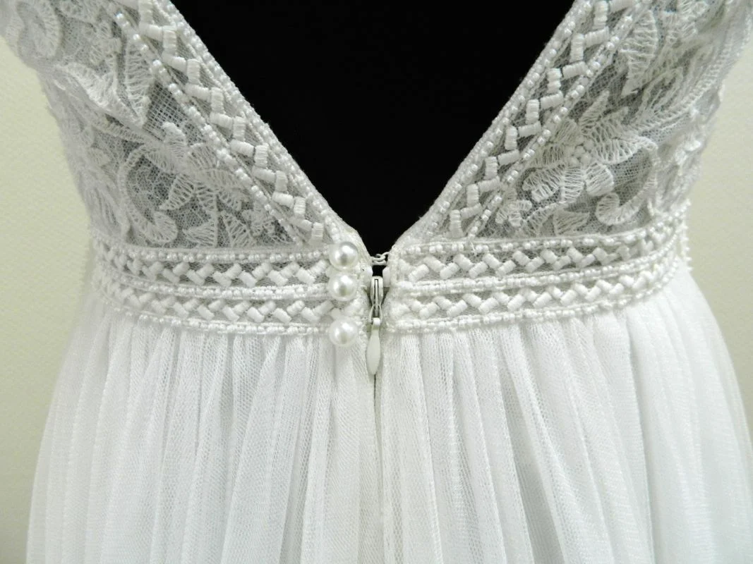 Gros plan sur le décolleté dos nu en V de la robe de mariée princesse Ululan de Rosa Clará, mettant en valeur la dentelle perlée, les boutons nacrés et la ceinture tressée.