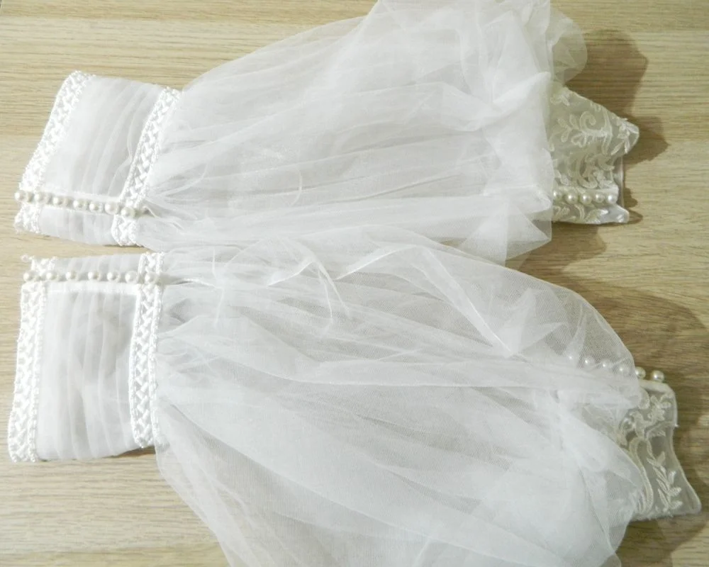 Gros plan à plat sur les manches amovibles bouffantes en tulle transparent et poignets en dentelle perlée de la robe de mariée princesse Ululan de Rosa Clará.