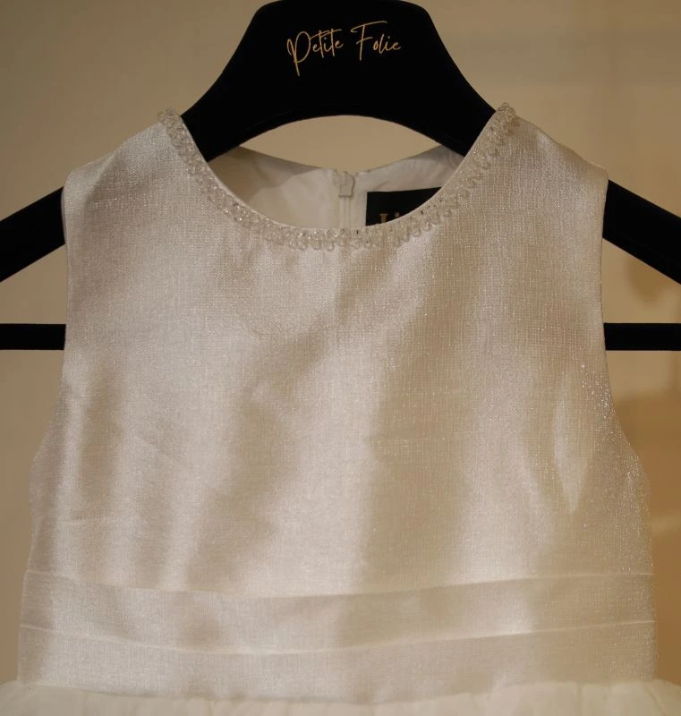 Gros plan sur le bustier en satin brillant, la ceinture plissée et l'encolure perlée de la robe fillette de cérémonie Anouk.
