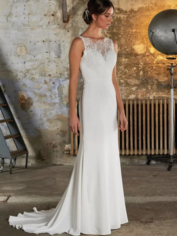 Une robe de mariée ajustée avec un décolleté illusion en dentelle, sans manches, et une traîne fluide. Le cadre industriel en arrière-plan met en valeur l'élégance contemporaine de la robe