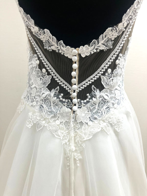 Gros plan sur le dos illusion en dentelle florale et les boutons perlés de la robe de mariée Très Chic 23419.