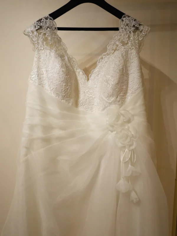 Gros plan sur le bustier en dentelle florale délicate d'une robe de mariée, montrant les détails des broderies et les finitions perlées sur un portant.
