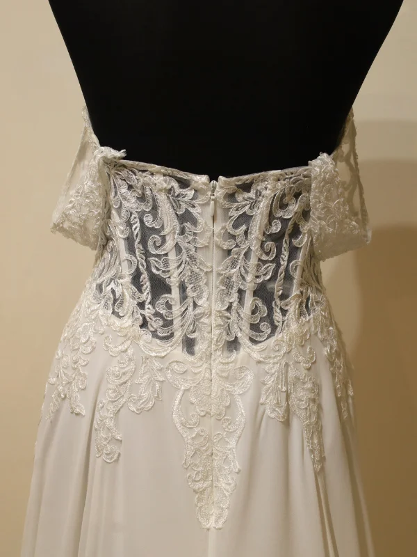 Gros plan sur le dos de cette robe de mariee sur portant, mettant en valeur la transparence de la dentelle illusoire et l'élégance de la fermeture éclair centrale