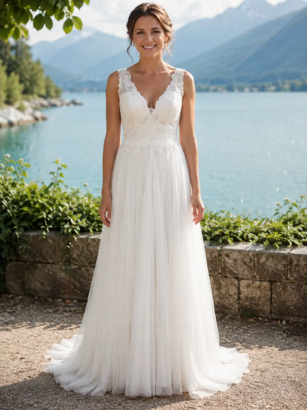 Robe de mariée Cachou par Cymbeline vue de face au bord d'un lac, mettant en avant son col en V, ses bretelles en dentelle rebrodée et sa jupe en tulle vaporeux.