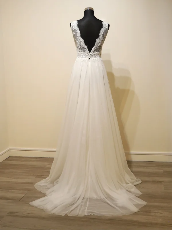 Vue de dos de la robe de mariée Cachou signée Cymbeline sur mannequin dans un showroom, mettant en avant le dos nu orné de dentelle fine, la rangée de boutons perlés et la traîne élégante en tulle.